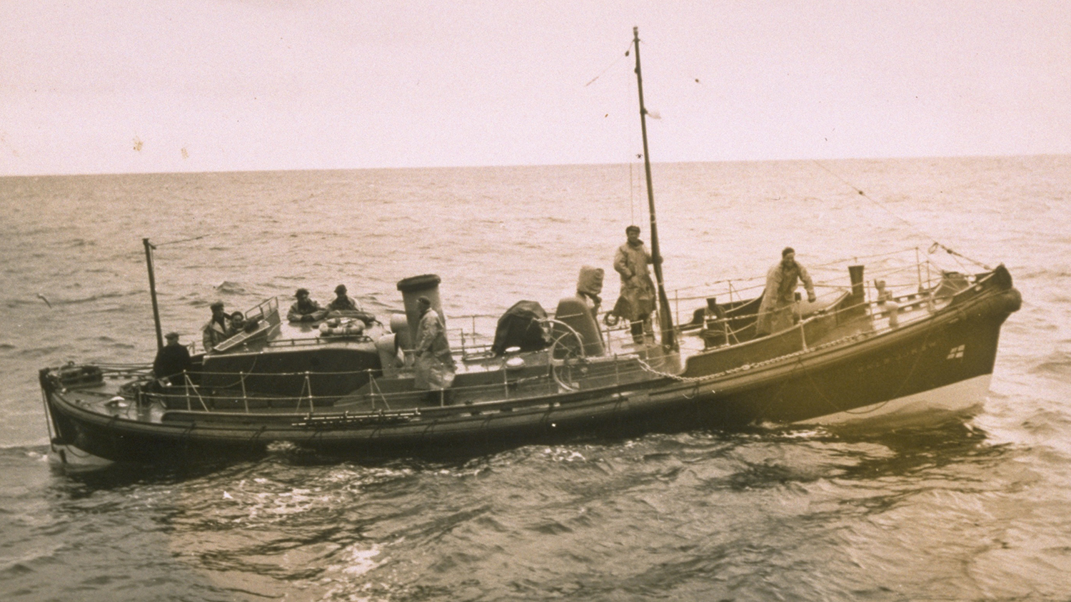 A black and white photograph showing a broadside view of Stromness’s Barnett class lifeboat, with five crew on deck. 
