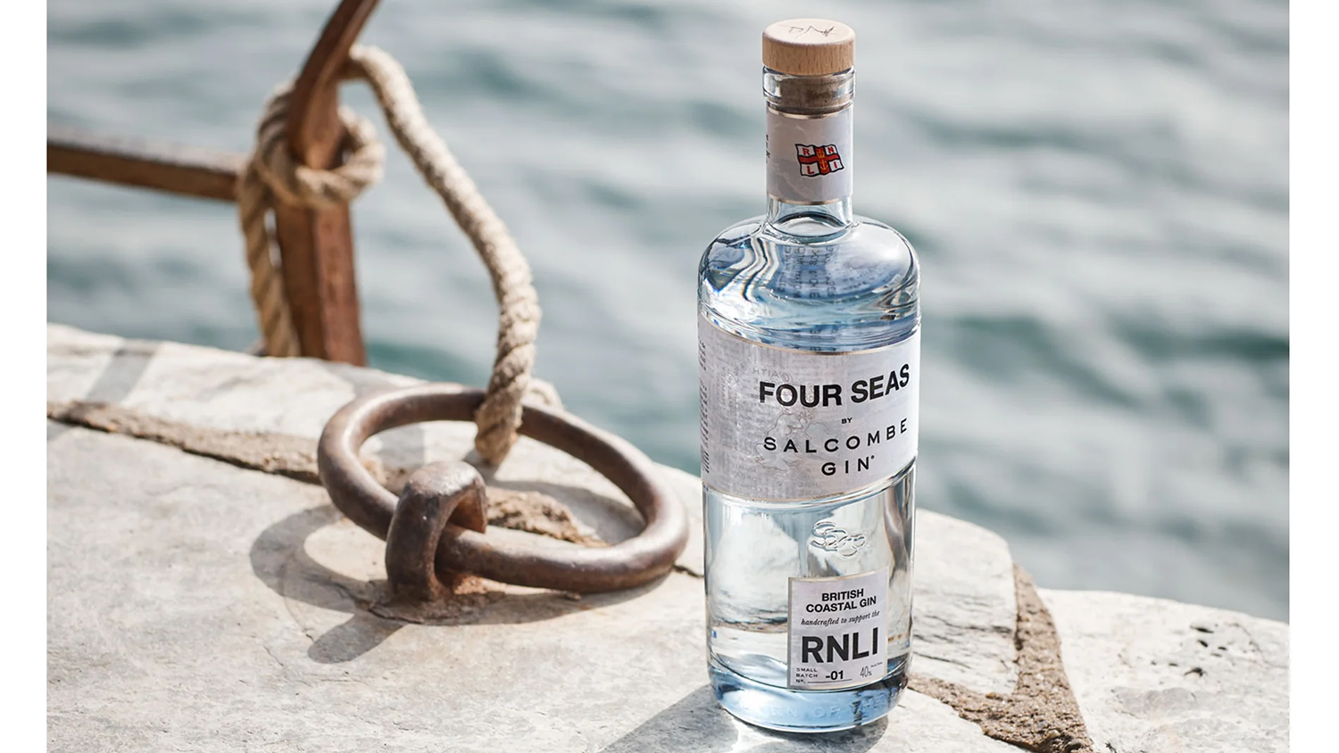 A bottle of Salcombe Gin’s Four Seas gin rests on a harbour wall next to a mooring ring