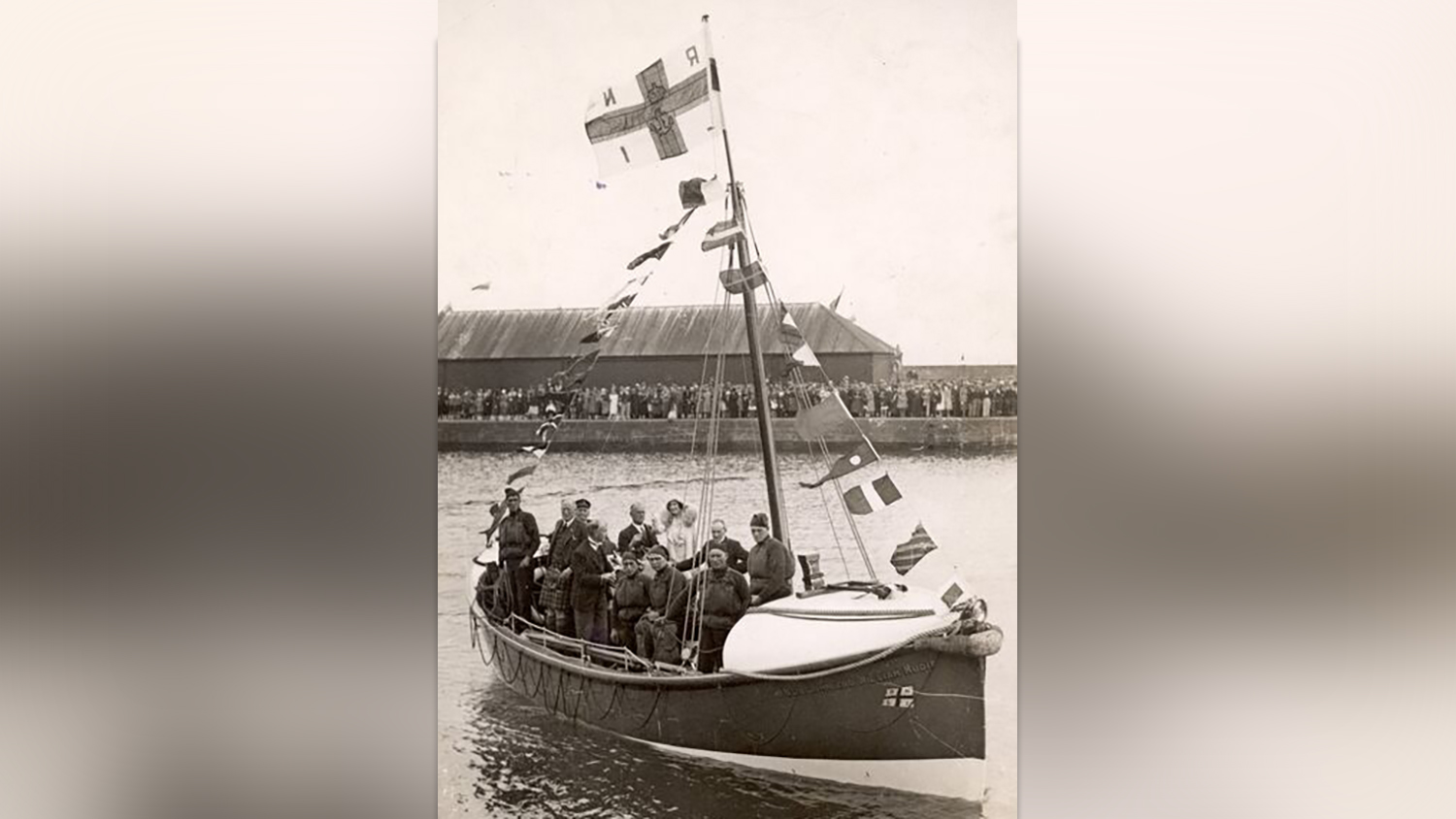 A black and white photograph of Queen Elizabeth the Queen Mother onboard Arbroath’s motor lifeboat, alongside her crew. 