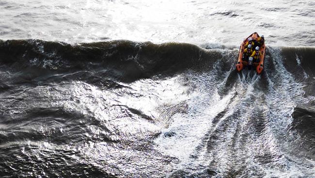 Aerial photo looking down on an RNLI D class lifeboat as it breaks through a wave on an overcast day