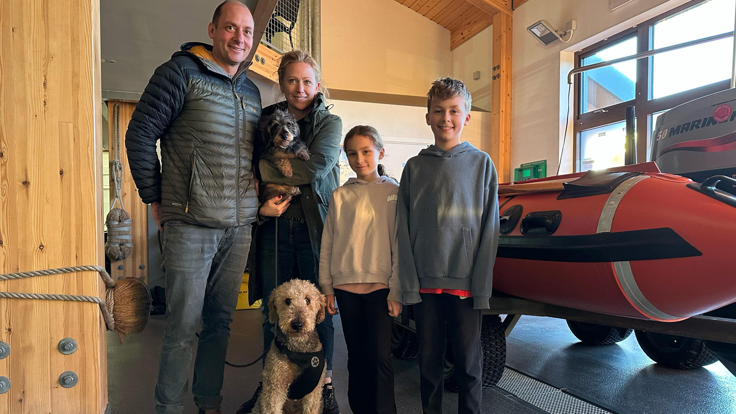 Olive the dog poses with her family (dad, mum, boy, girl and another dog) inside the boathouse at Wells Lifeboat Station