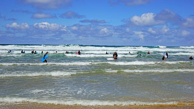 Bodyboarders and swimmers in the north Cornwall surf – the view from the sandy beach on a sunny day with a smattering of clouds.