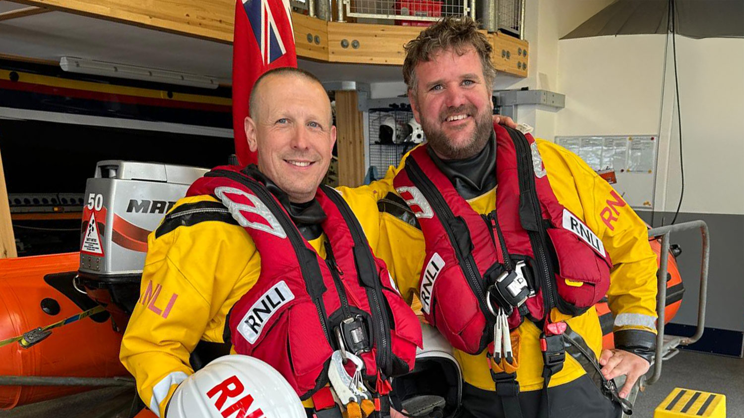 Wells lifeboat crew members Simon Parkes and Gary Yarham stand next to a D class lifeboat inside a boathouse