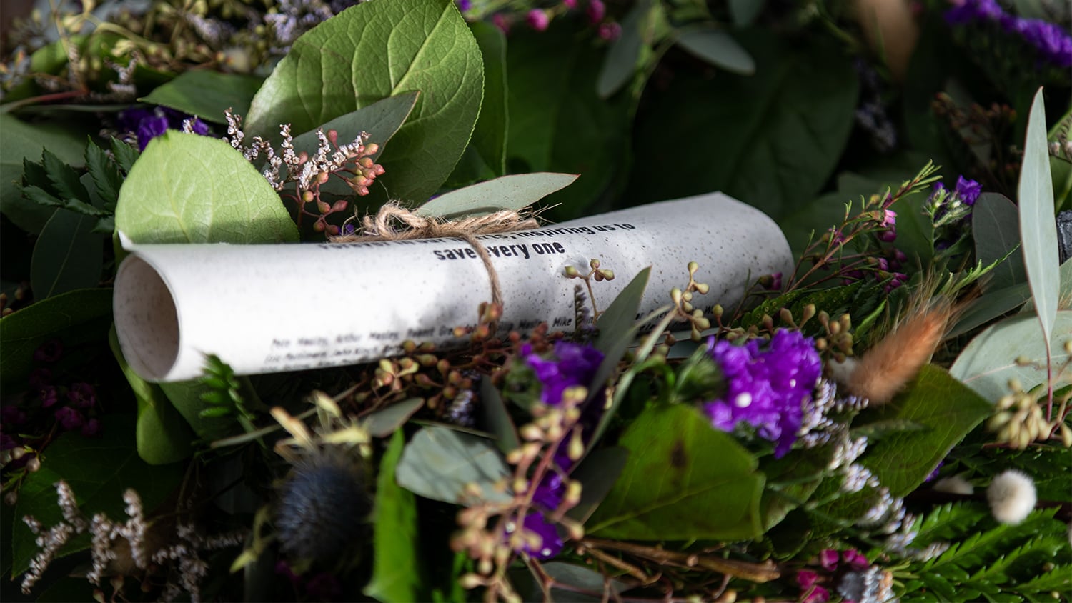 A marine-friendly scroll with the names of supporters’ loved ones tied to a wreath of green leaves and purple flowers. Photo: RNLI/Charlotte Hill
