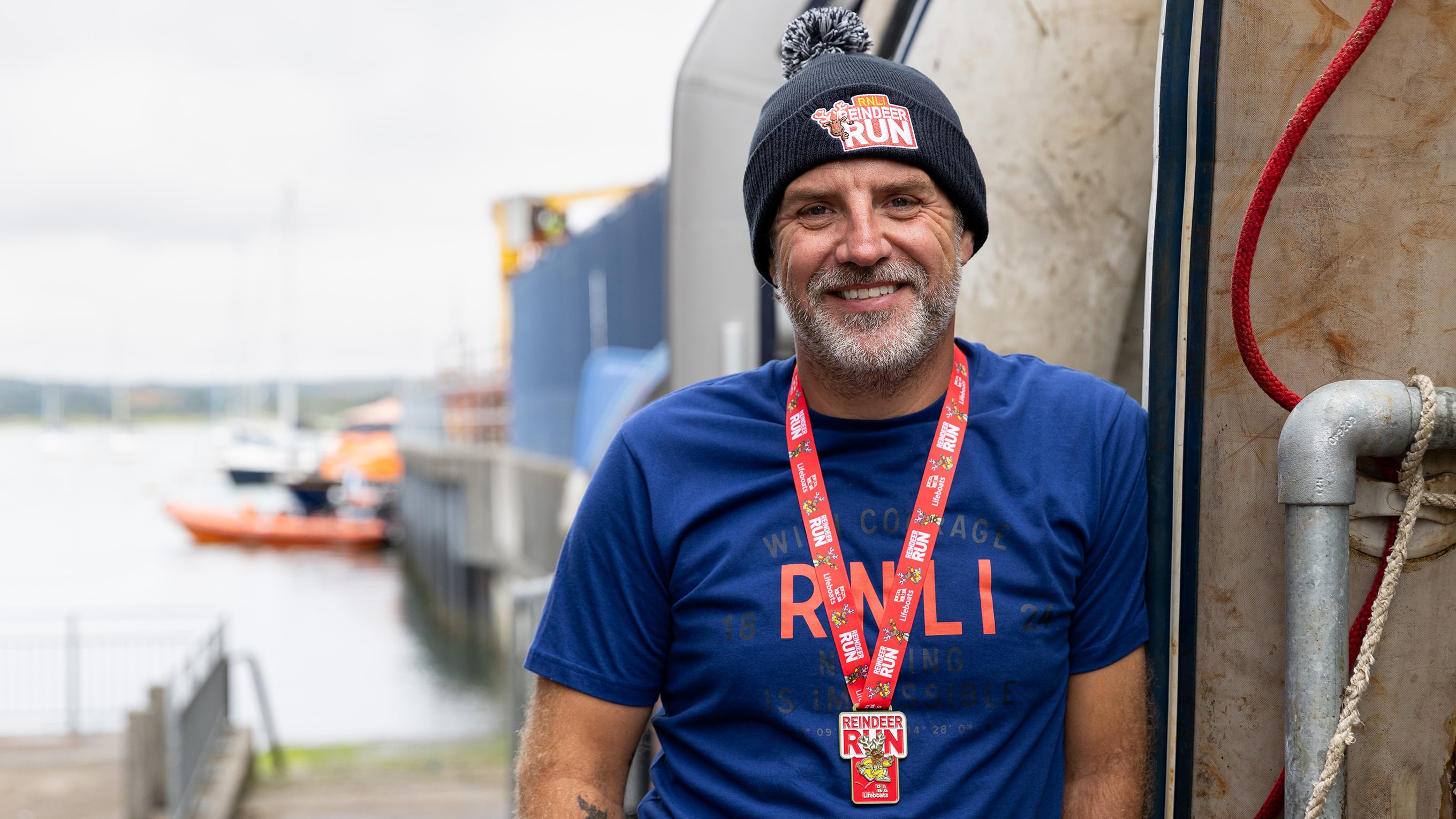 A runner who has taken part in the Reindeer Run, wearing a navy RNLI T-shirt, dark Reindeer Run beanie and red medal. Photo: RNLI/Nathan Williams.