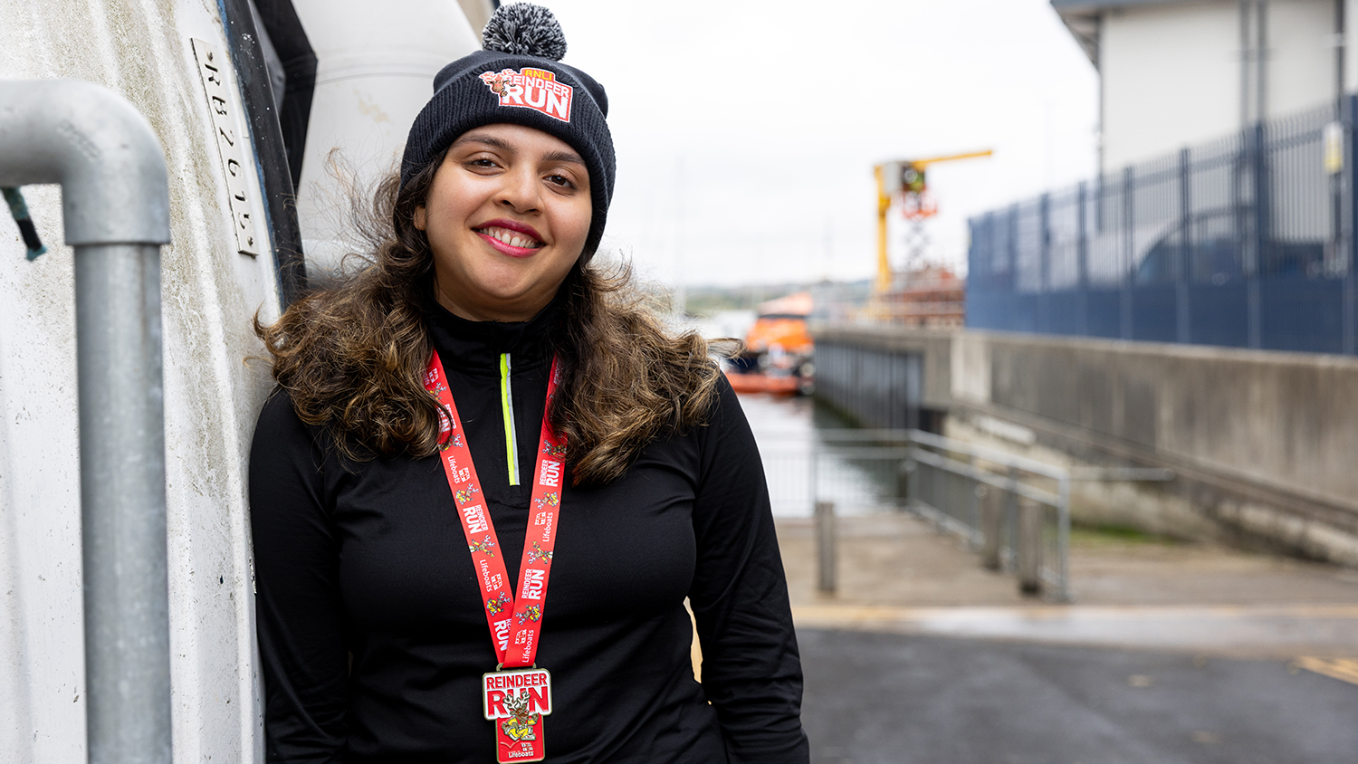 A woman wearing a Reindeer Run beanie and medal, smiling at the camera.