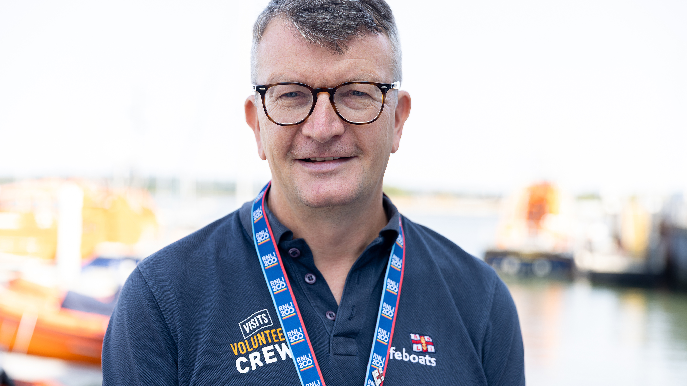 Alt text: Stuart Lindsay, a volunteer tour guide at the RNLI College, smiles at the camera. He’s wearing a dark blue RNLI volunteer polo shirt. RNLI/Nathan Williams.