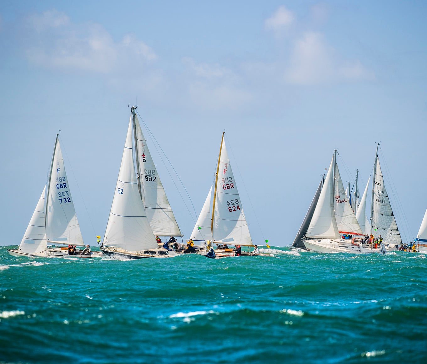 A group of yachts in a race, in turquoise seas and beneath blue sky.