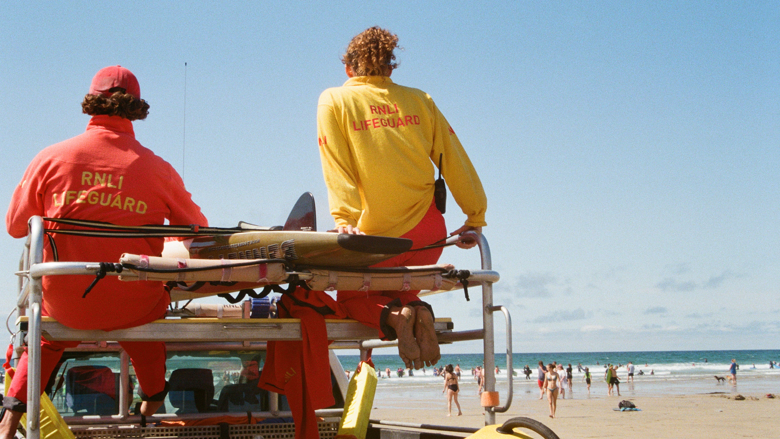Two RNLI lifeguards sit on an all-terrain vehicle, looking out to sea.
