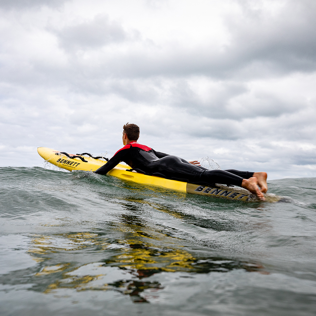 A lifeguard swimming out to sea on a rescue board.