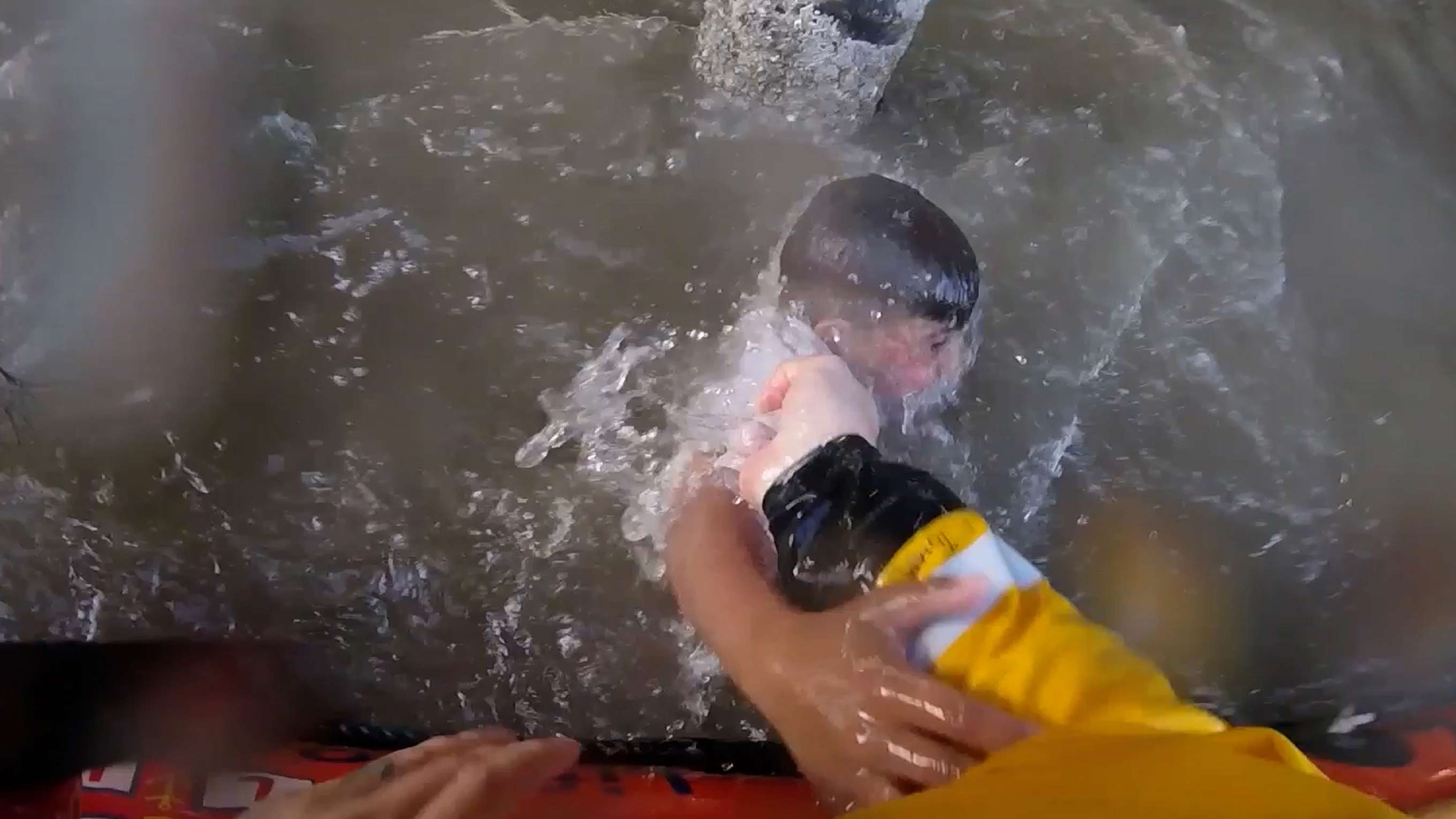 Point of view from a lifeboat crew member wearing bright yellow lifeboat kit as they pull a drowning boy from underneath the water and into the safety of the lifeboat