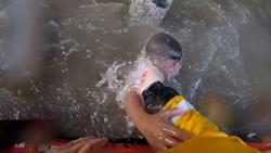 Point of view from a lifeboat crew member wearing bright yellow lifeboat kit as they pull a drowning boy from underneath the water and into the safety of the lifeboat
