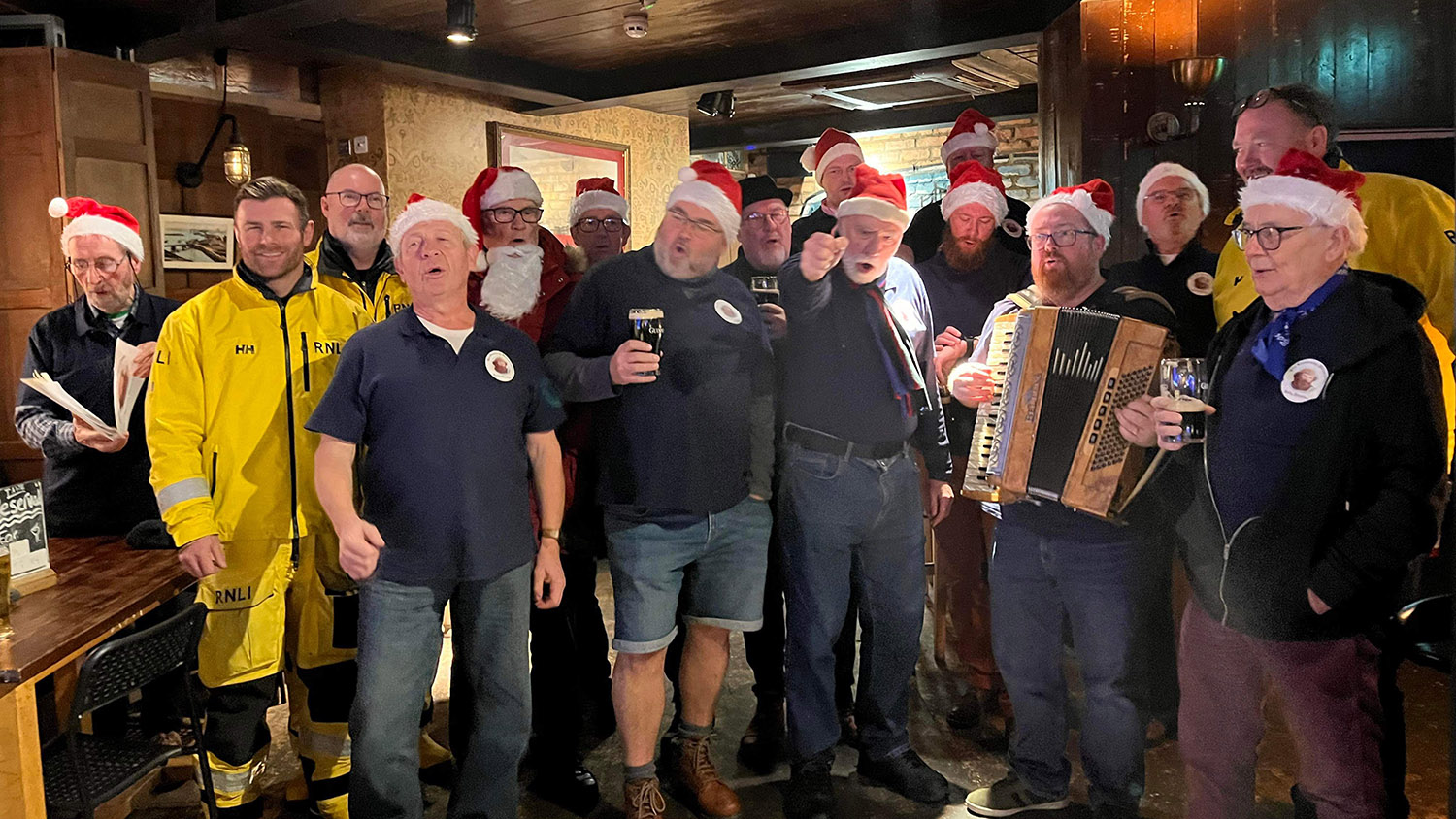 The Causeway Shantymen are singing together, wearing Santa hats. 