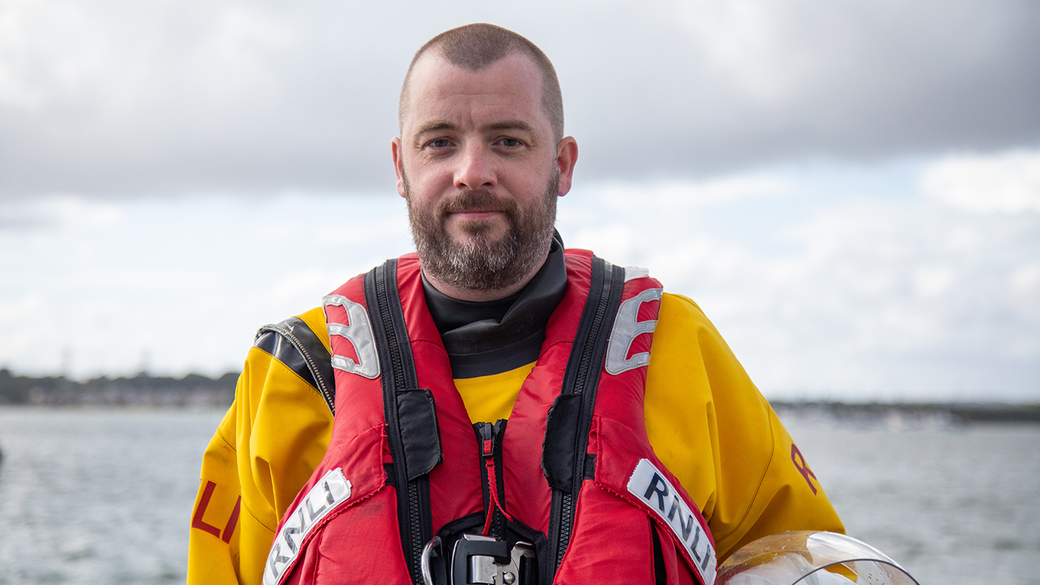 A head and shoulders shot of Rhyl RNLI Volunteer Lifeboat Crew Member Colin Jones in crew kit with the sea in the background.