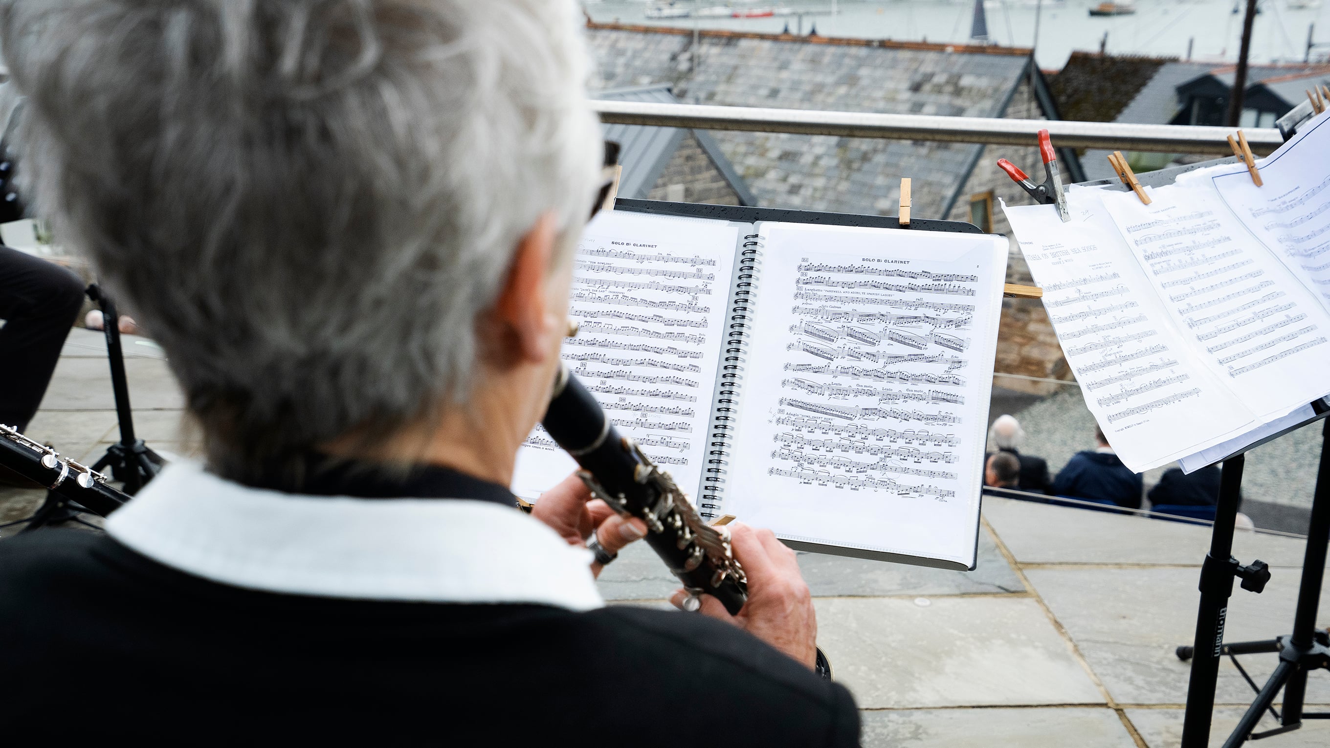 A musician is playing a clarinet. The photograph is taken from behind, so you can see the sheet music she is following. Photo: RNLI/Nigel Millard.