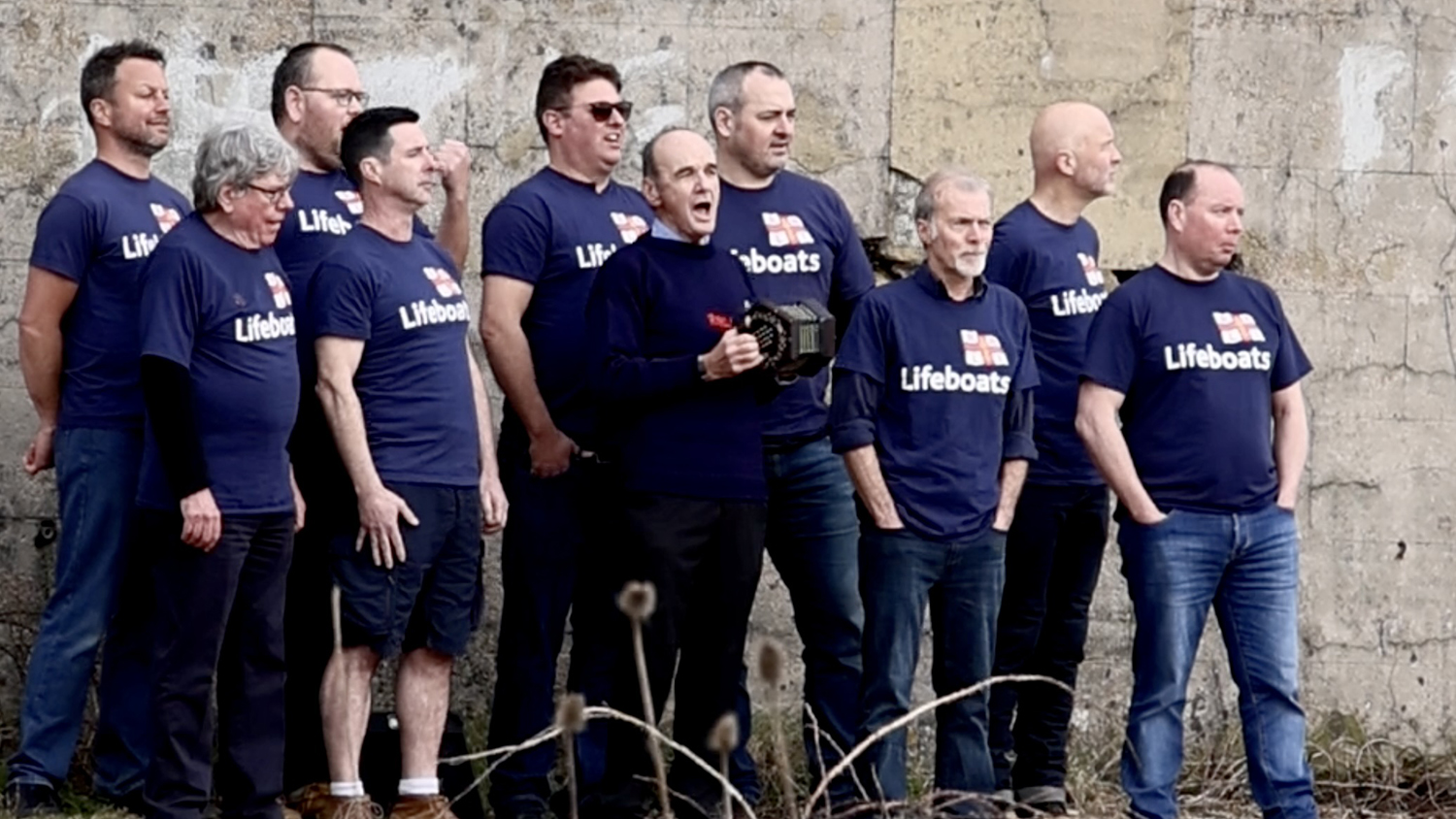 The Dockyard Dogs singing together, all wearing navy RNLI T-shirts.
