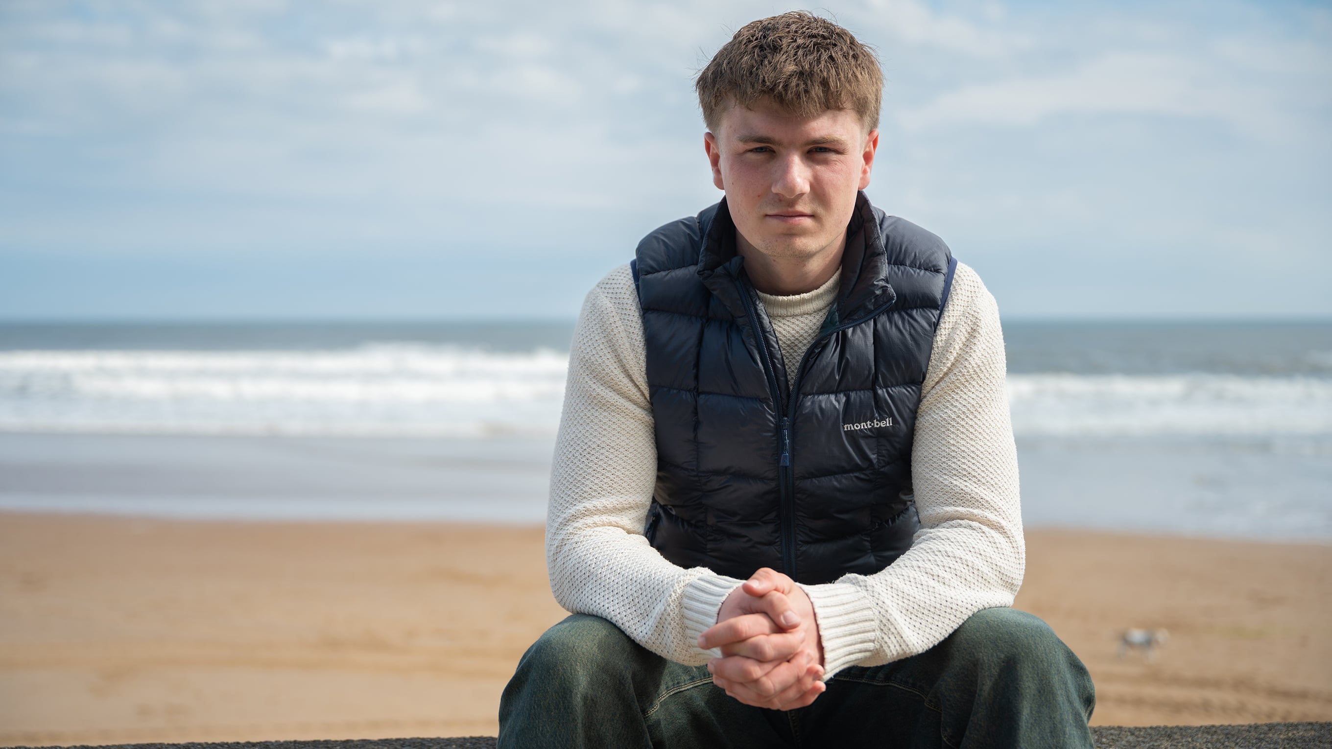A portrait of Euan, who was rescued by the RNLI, sitting at the beach. He’s staring directly at the camera. Photo: RNLI/James Moffatt.