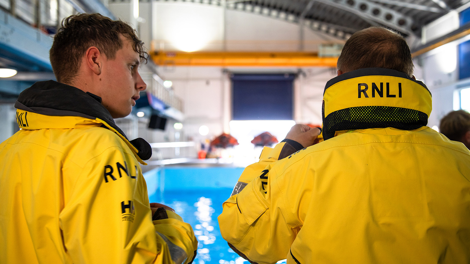 The back of father and son Burnham-on-Sea RNLI Crew Members Jason and Jake Coombes as they discuss their training. The RNLI Sea Survival Pool is in the background.