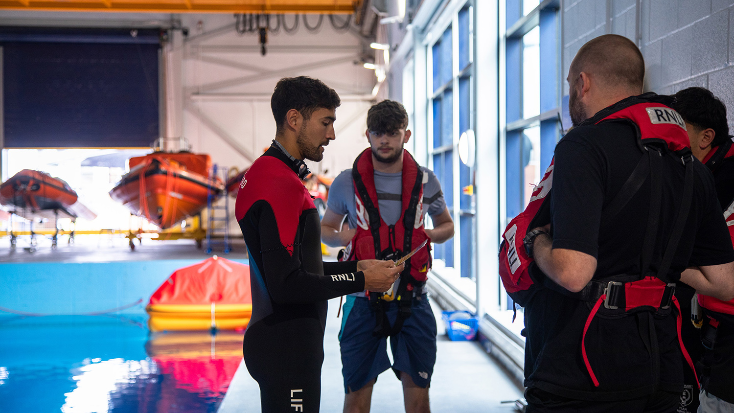 Father and son Rhyl Crew Members Colin and Rhys Jones at the side of the RNLI Sea Survival Pool listening to one of the trainers.