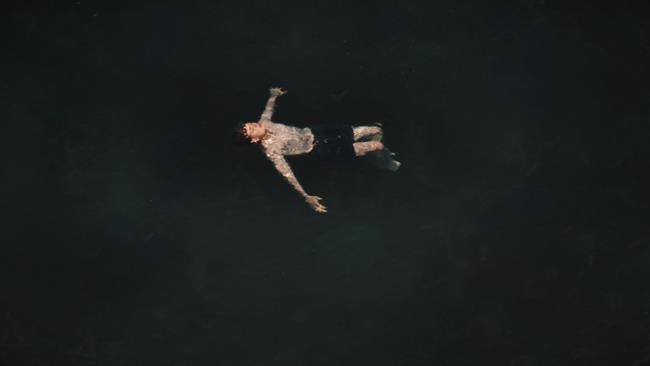 A still from the RNLI and GAA’s Float to Live film, showing a teenage boy floating in a dark sea. He has his arms outstretched and his head tilted back.
