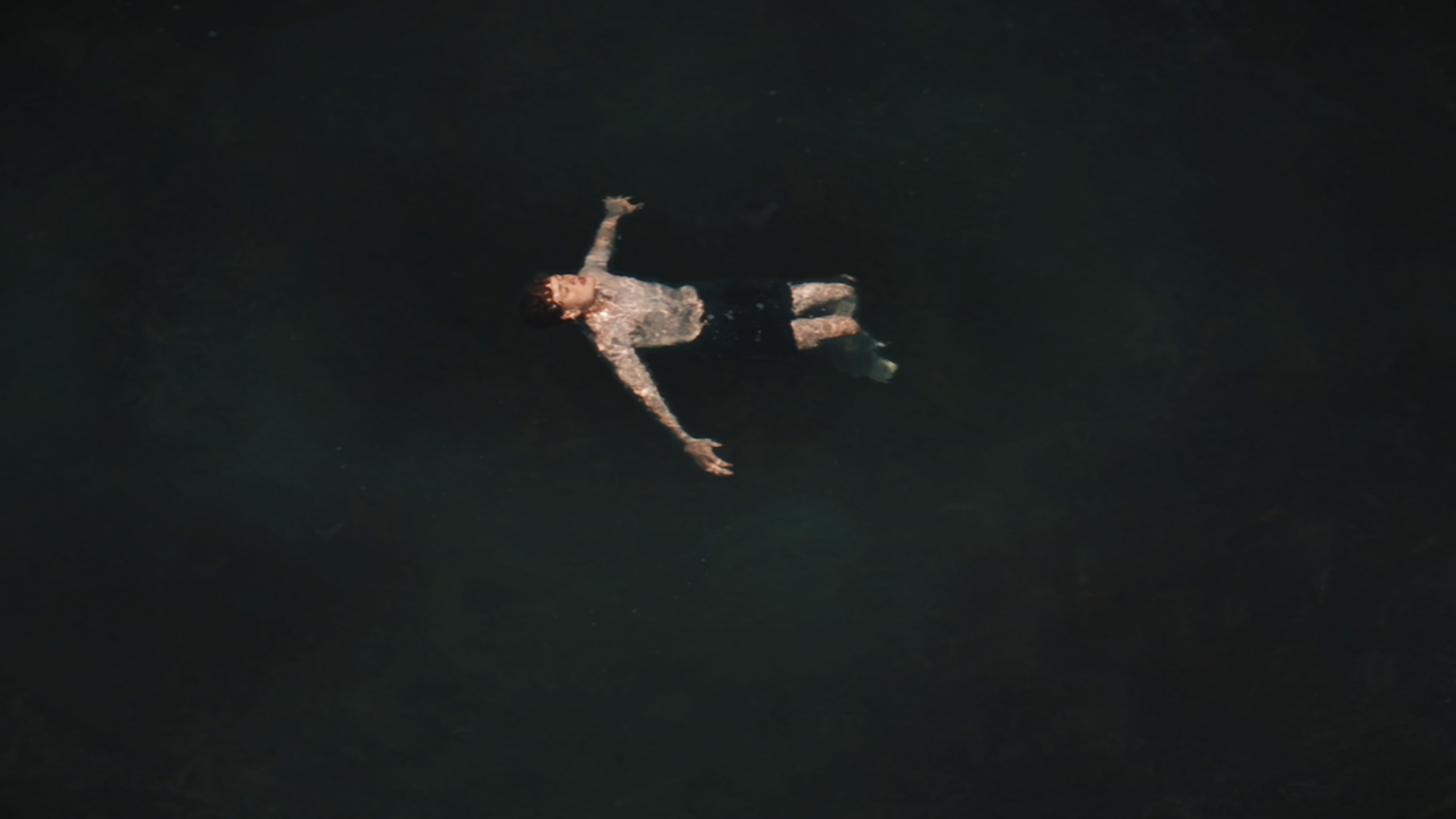 A still from the RNLI and GAA’s Float to Live film, showing a teenage boy floating in a dark sea. He has his arms outstretched and his head tilted back.