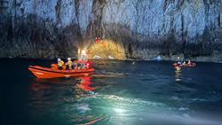 A nighttime image of a B class lifeboat and a D class lifeboat floating on the water next to an incident at the base of some cliffs. A spotlight illuminates HM Coastguard volunteers in bright orange jumpsuits as they tend to a casualty.