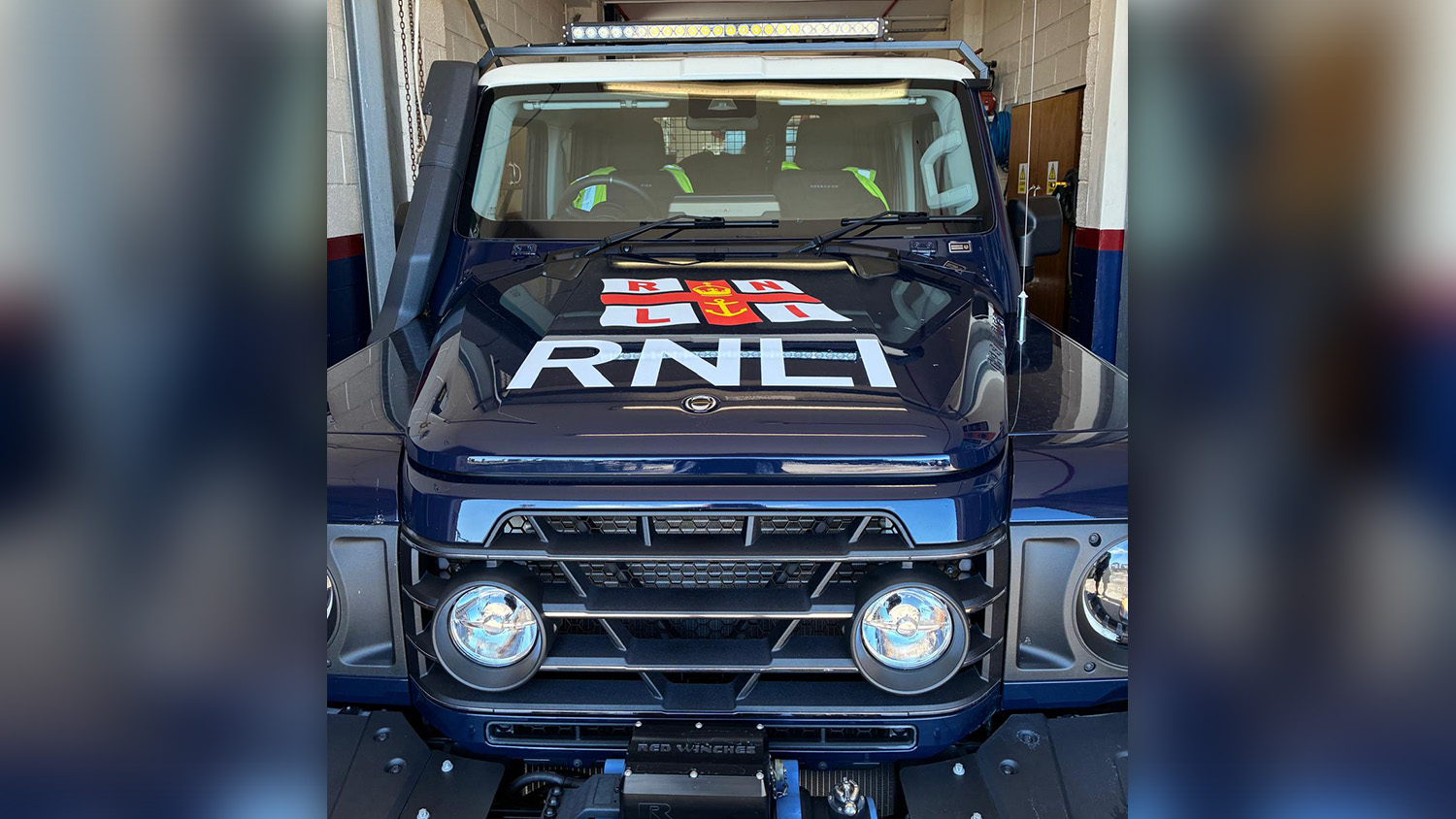 A close-up of the front of the INEOS Grenadier. It’s a navy-blue vehicle with the RNLI’s logo across the front. 