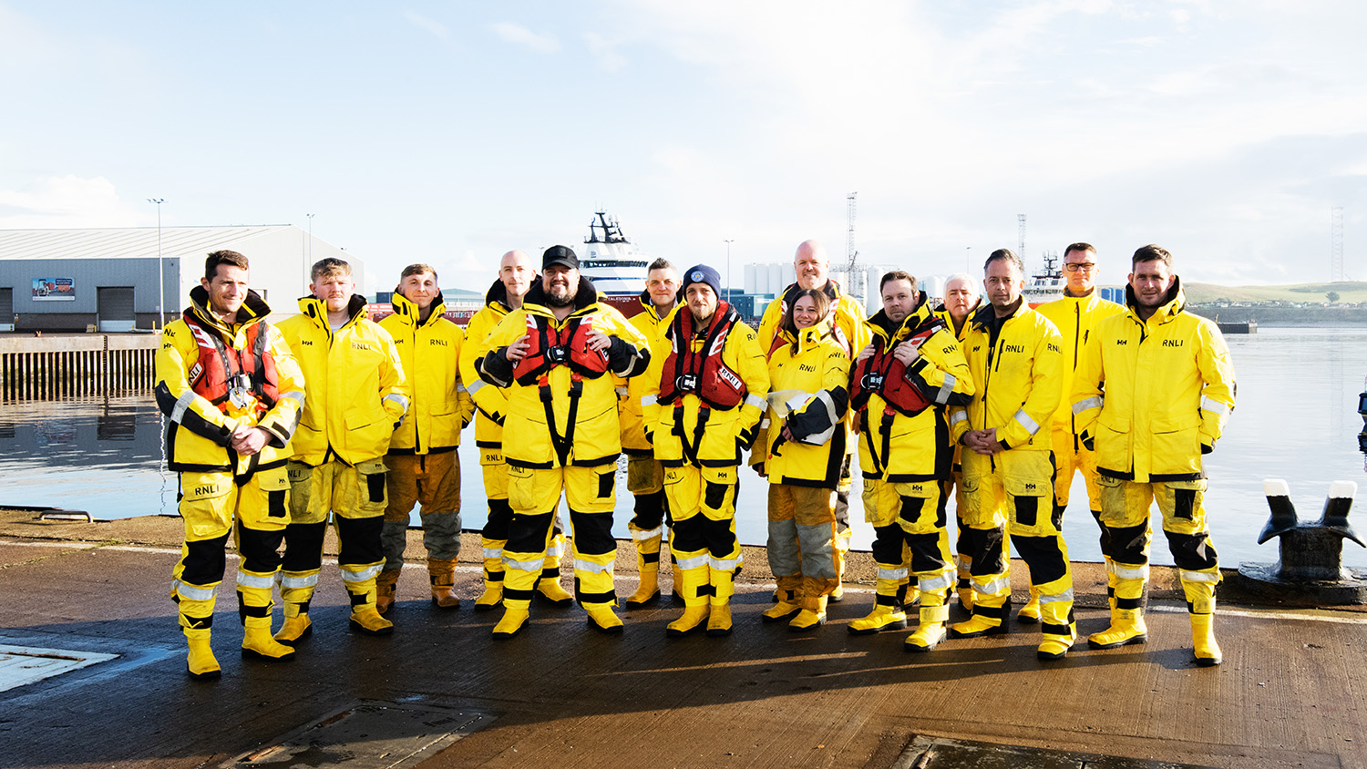 Aberdeen RNLI volunteer crew members standing on the quayside on a sunny day. They are all wearing crew kit.