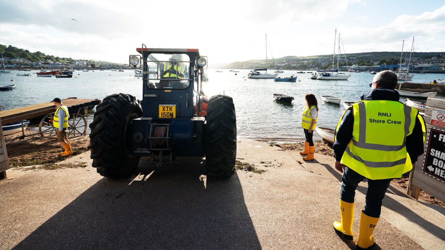 Shore crew marshall a tractor down a slipway.
