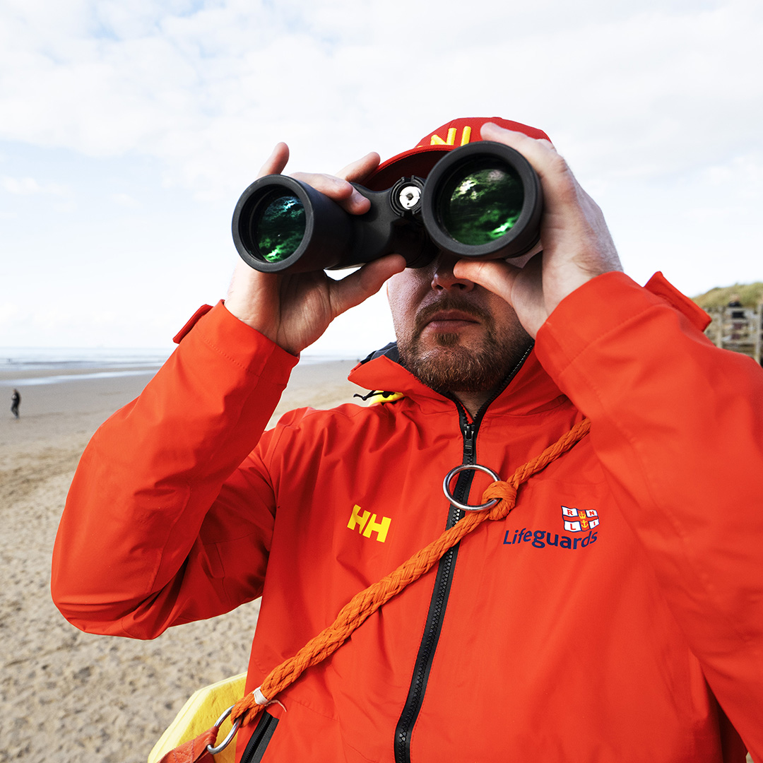 A lifeguard looking through a pair of binoculars. 