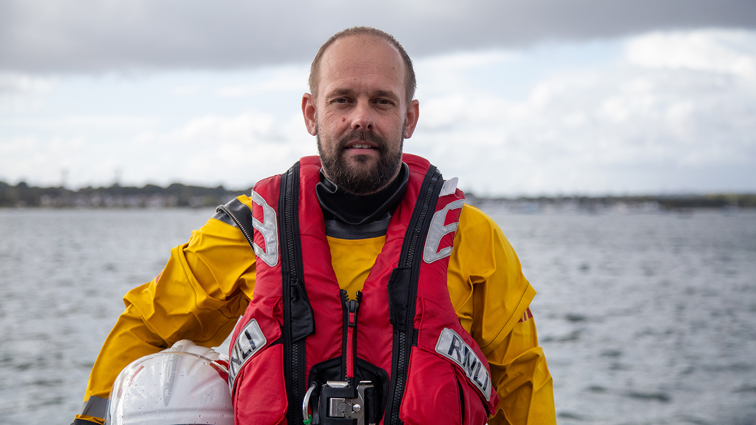 A head and shoulders shot of Burnham-on-Sea RNLI Volunteer Lifeboat Crew Member Jason Coombes in crew kit with the sea in the background.