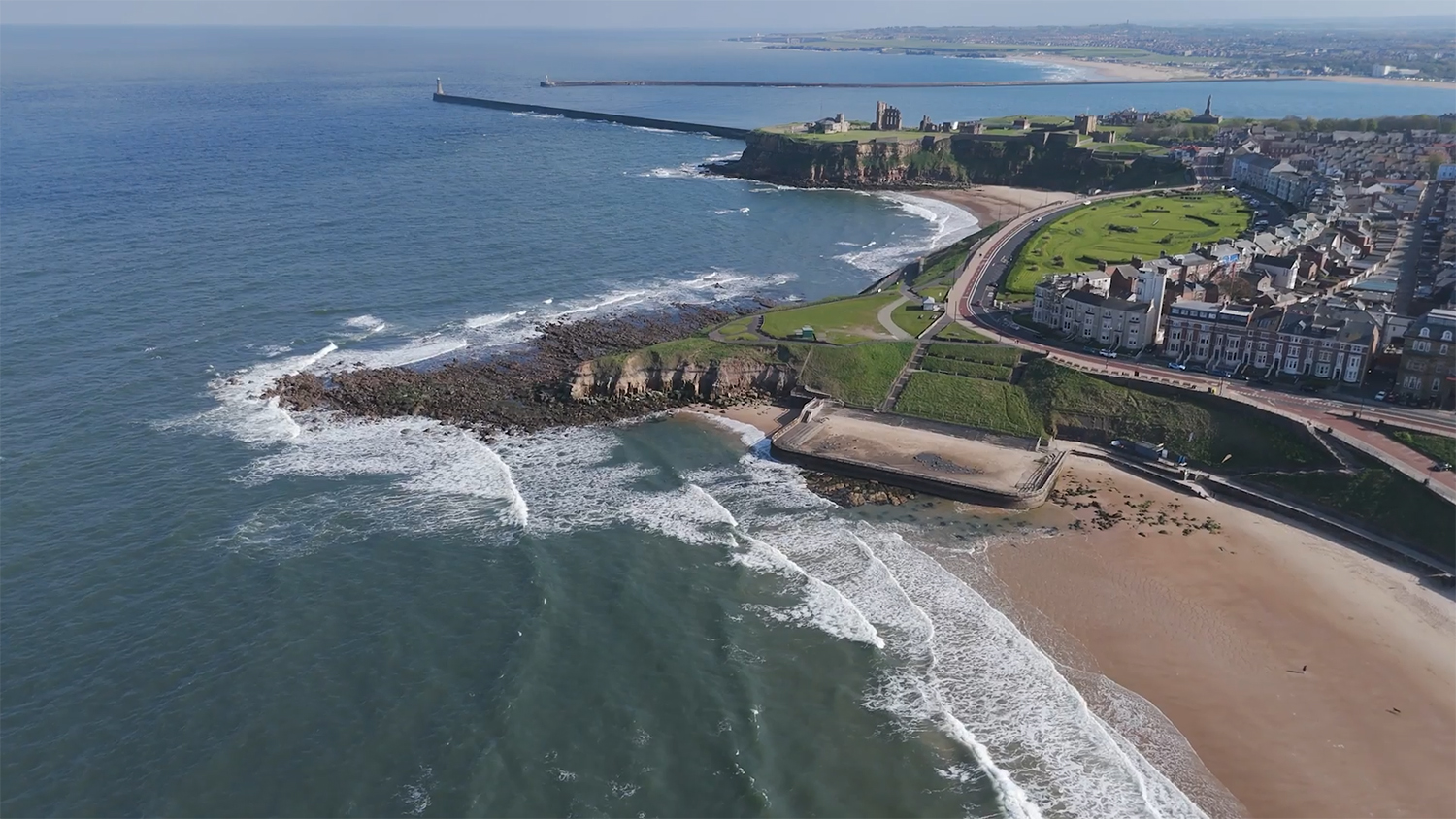 Longsands Beach, Tynemouth on a sunny day with blue skies. Waves are breaking along the shore. The photo has been taken from an aerial view.
