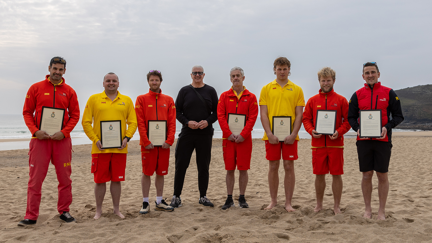 Rescuee Mark Ferrer at Praa Sands, standing with RNLI lifeguards, who are holding certificates.