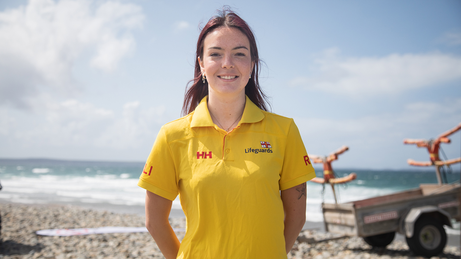 RNLI Lifeguard Anya Walton stands on a beach, smiling. 