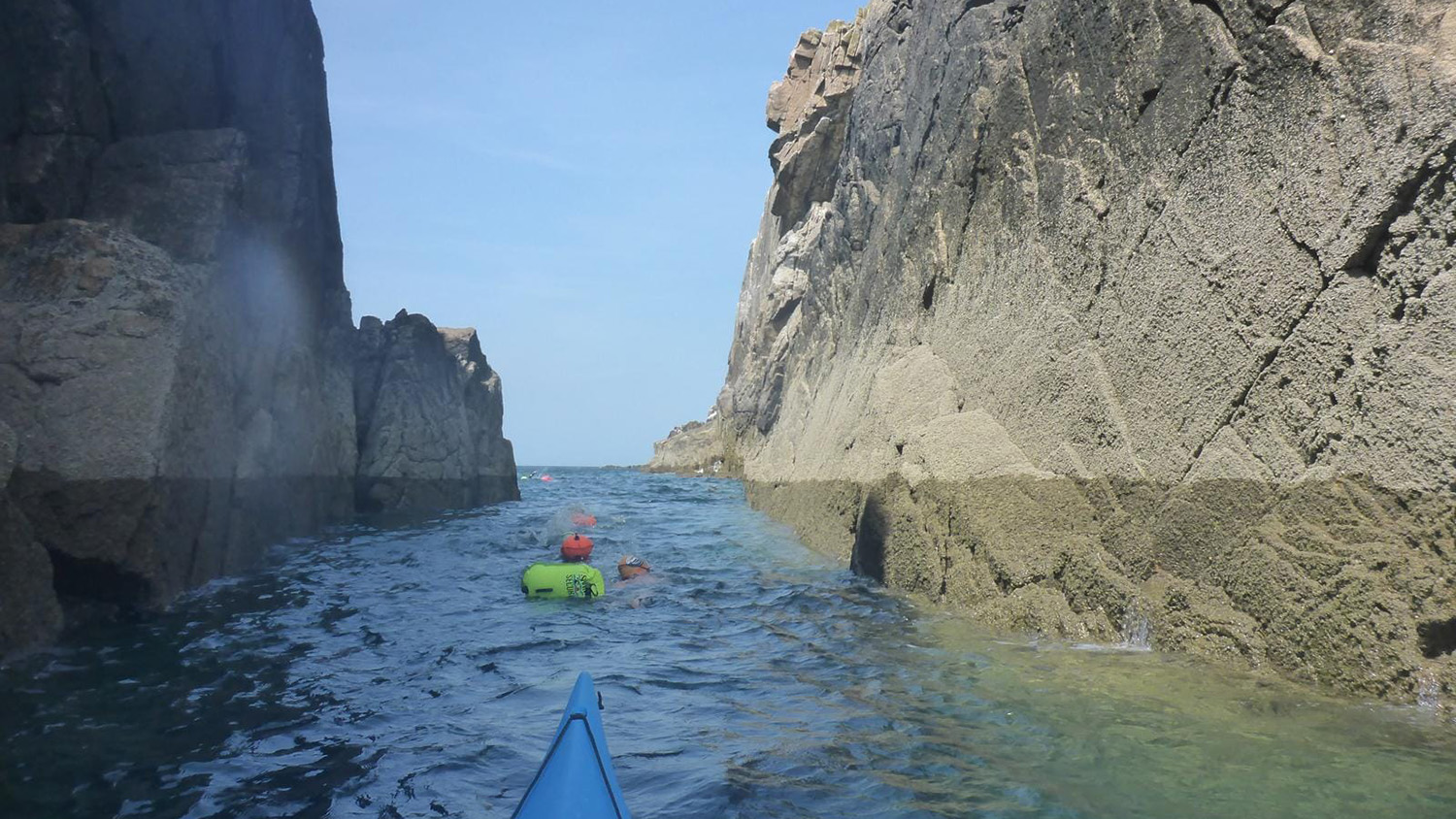 The view from a kayak, showing a swimmer, wearing a brightly coloured cap and tow float, in the sea.