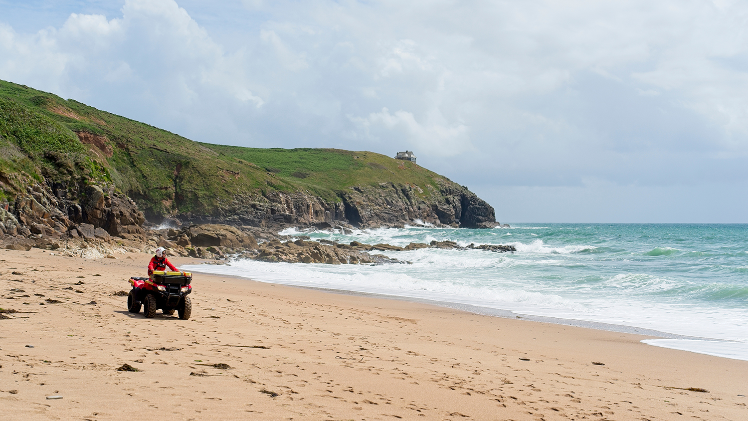 An RNLI lifeguard drives an all-terrain vehicle (ATV) at Praa Sands, Cornwall.