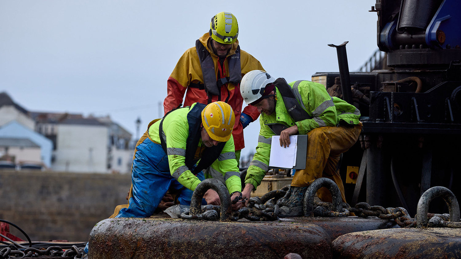 Three workers from Falmouth Diving are inspecting the chains of a sinker. 