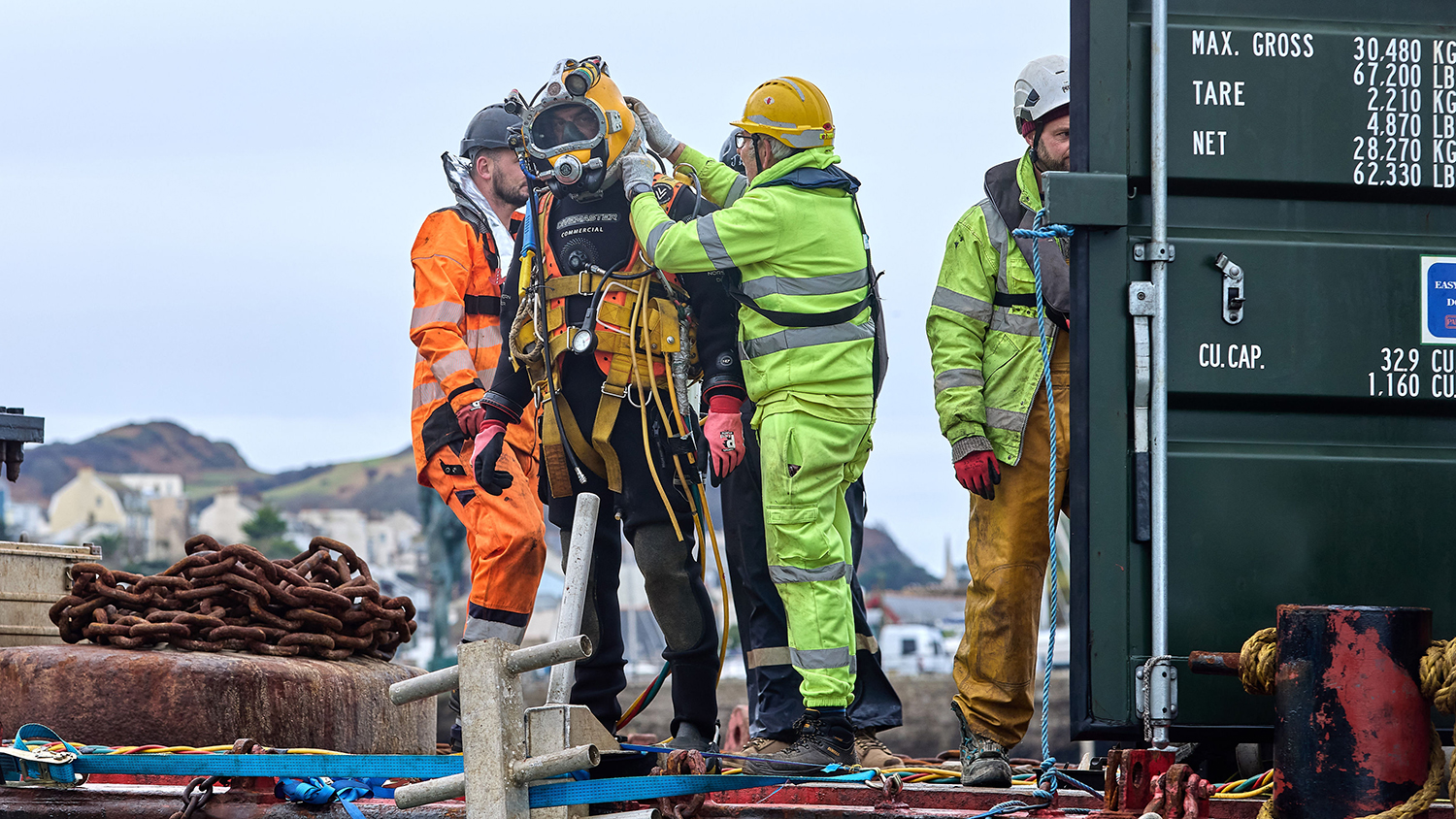 A diver is getting ready to inspect the mooring at Ilfracombe, with a group of people carefully checking his diving gear.  