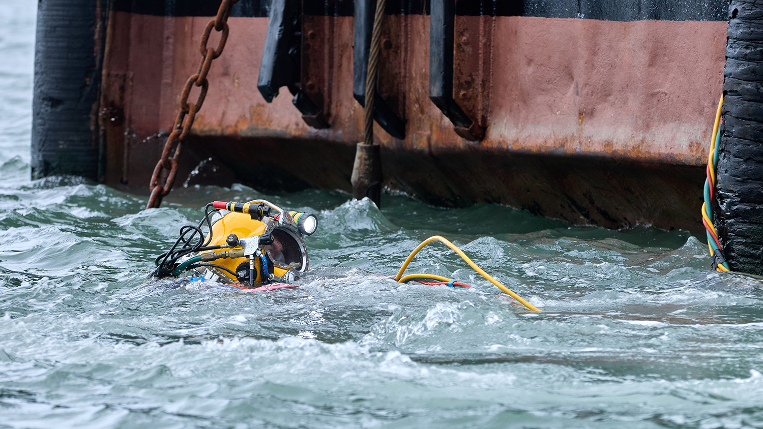 A diver is in the sea, with only his yellow diving helmet visible above the surface of the water.
