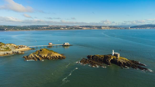 An aerial view of the two islands at Mumbles Head, showing a lighthouse situated on the more remote island. The Mumbles RNLI Lifeboat Station is in the background. Photo: Shutterstock.