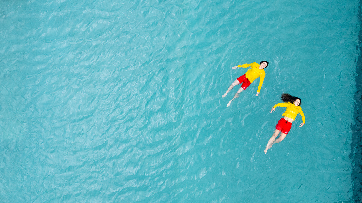 Two RNLI lifeguards float on their backs in water to demonstrate the lifesaving Float to Live technique. 