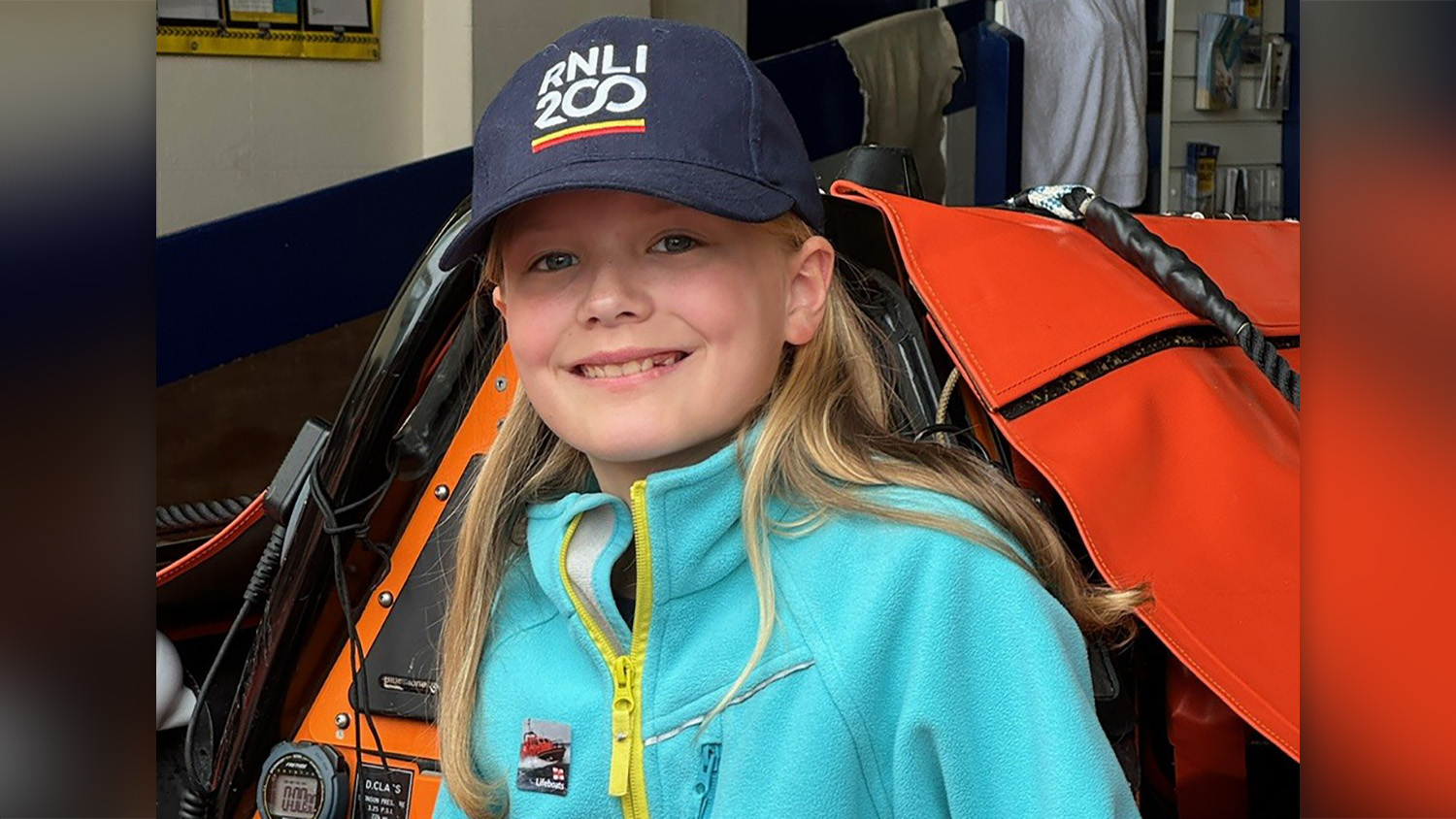 Tilly smiles at the camera, wearing an RNLI 200 navy cap. 