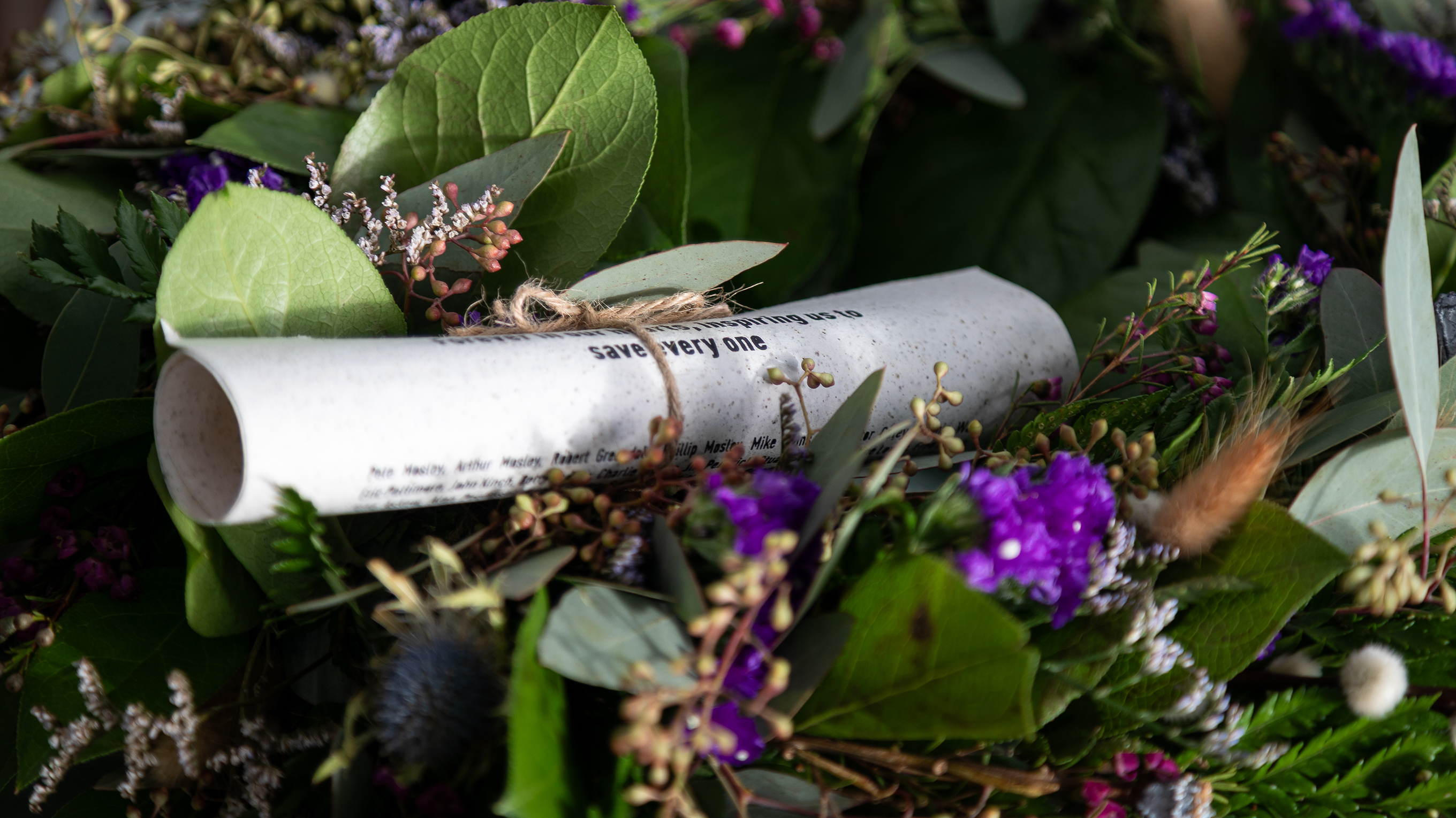 A marine-friendly scroll with the names of supporters’ loved ones tied to a wreath of green leaves and purple flowers. Photo: RNLI/Charlotte Hill