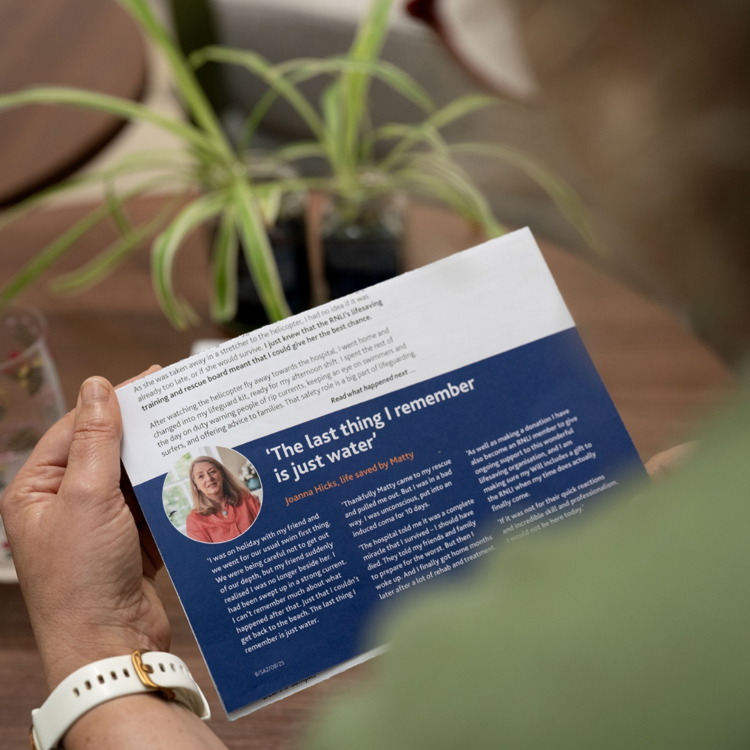 A woman reading an RNLI Summer Appeal leaflet featuring a real-life rescue story.