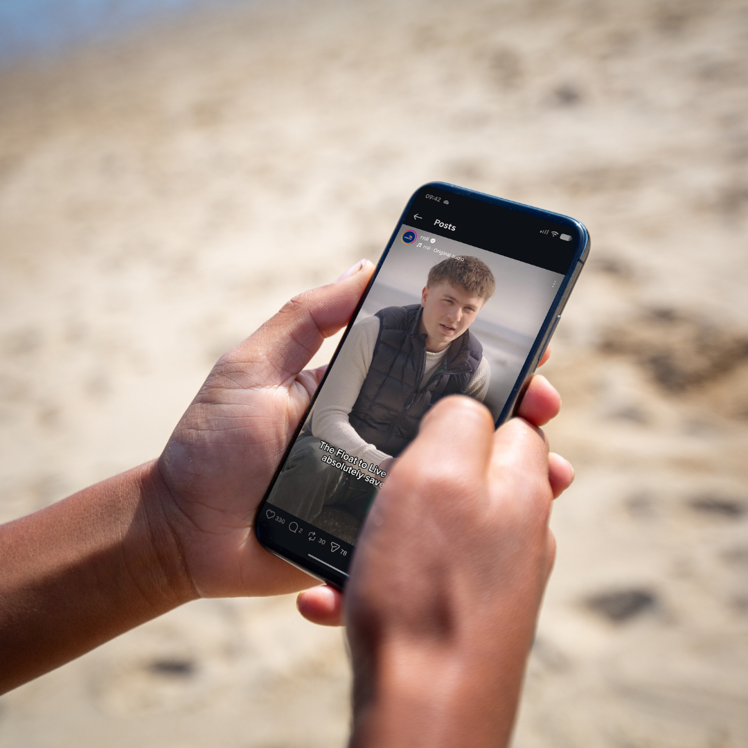 Hands holding a mobile phone displaying an RNLI Instagram post of a real-life rescue testimonial video..