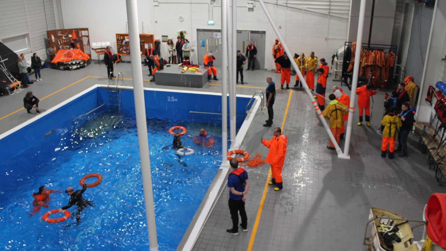 A group of participants take part in a man overboard training activity in an indoor pool