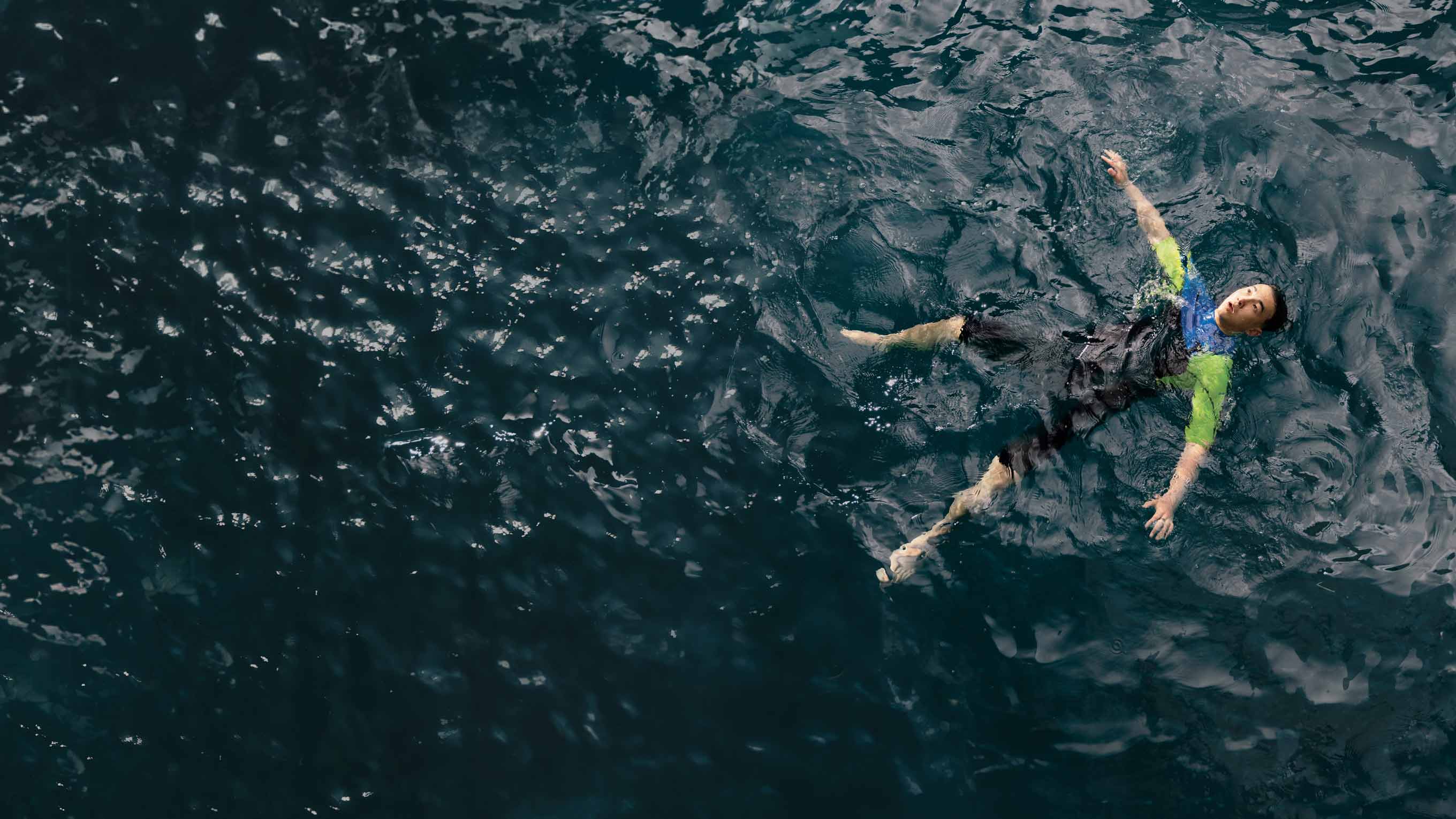 Overhead photo of a man in a wetsuit floating on their back in deep blue seas