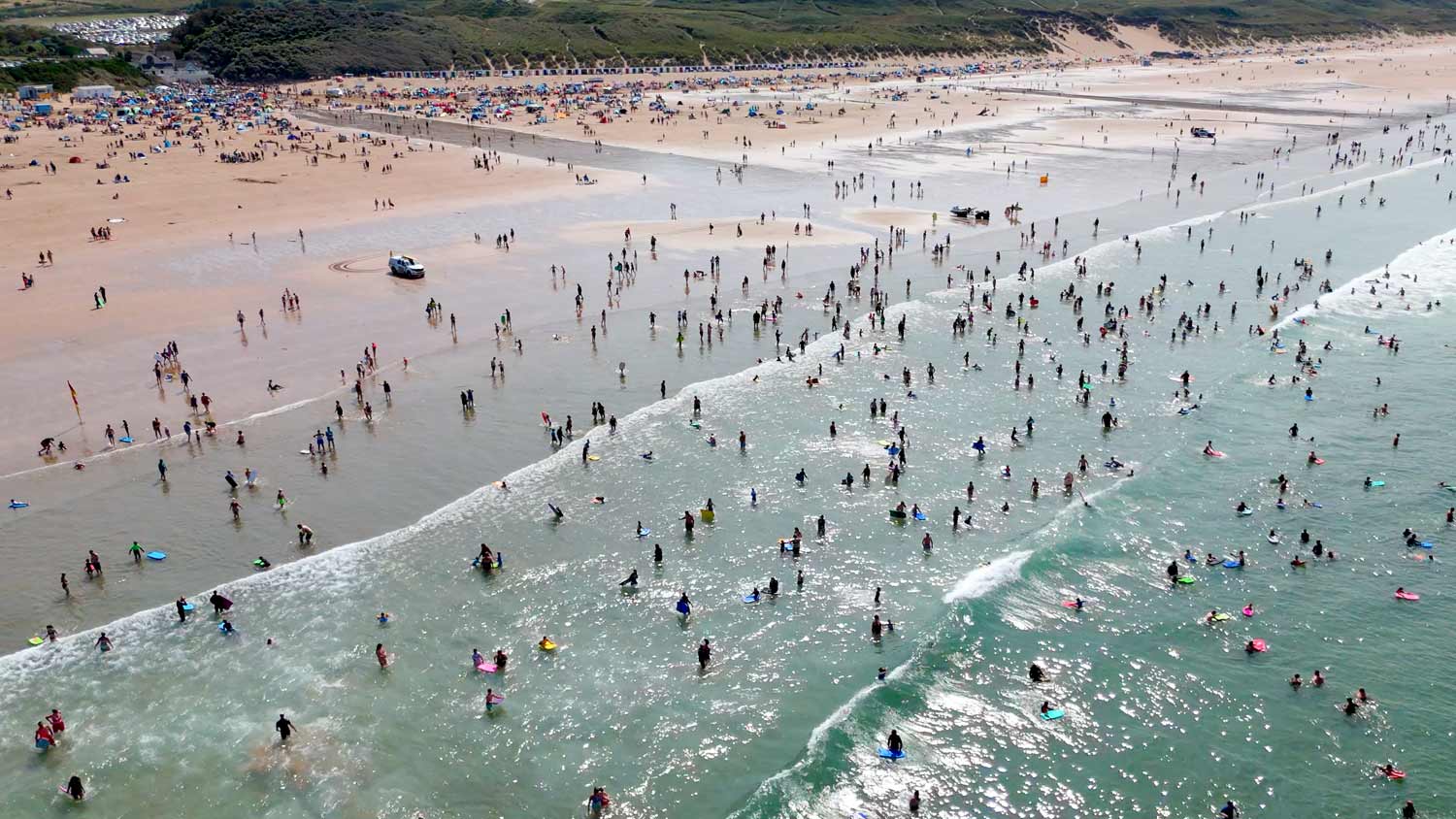 Aerial photo of a busy Woolacombe Beach where hundreds of people play in and out of the water