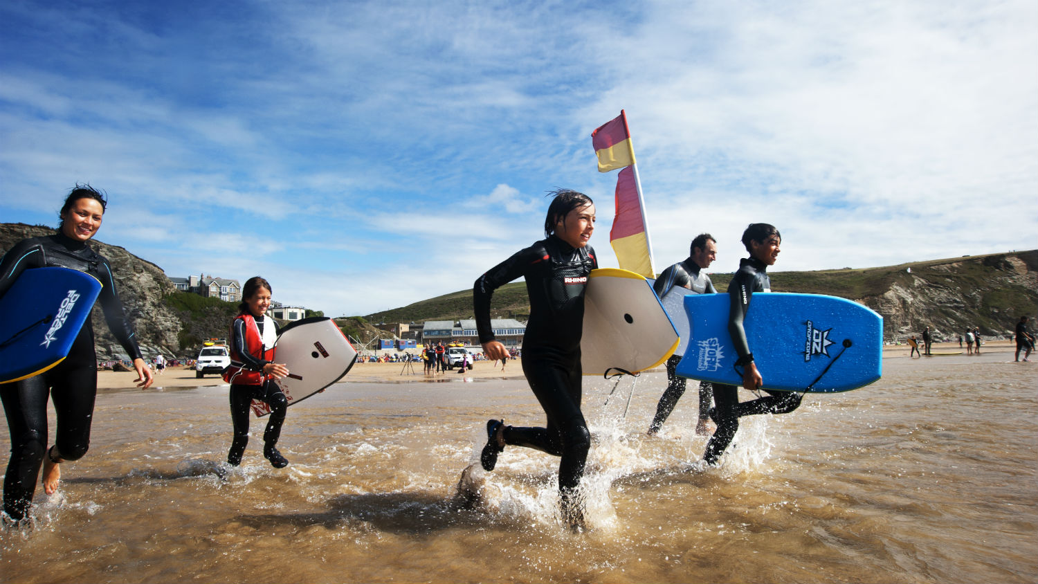 Family with bodyboards running into the surf in between the red and yellow flags