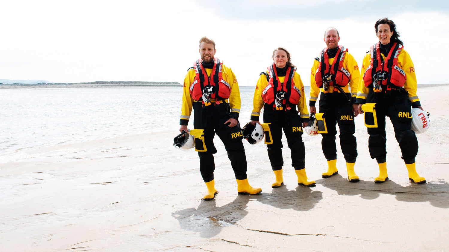 Four lifeboat crew members wearing inshore lifeboat kit stand together on a beach